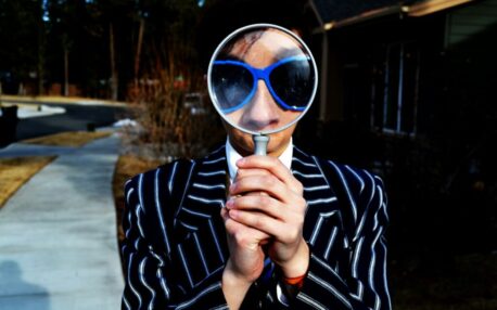 person using magnifying glass enlarging the appearance of his nose and sunglasses